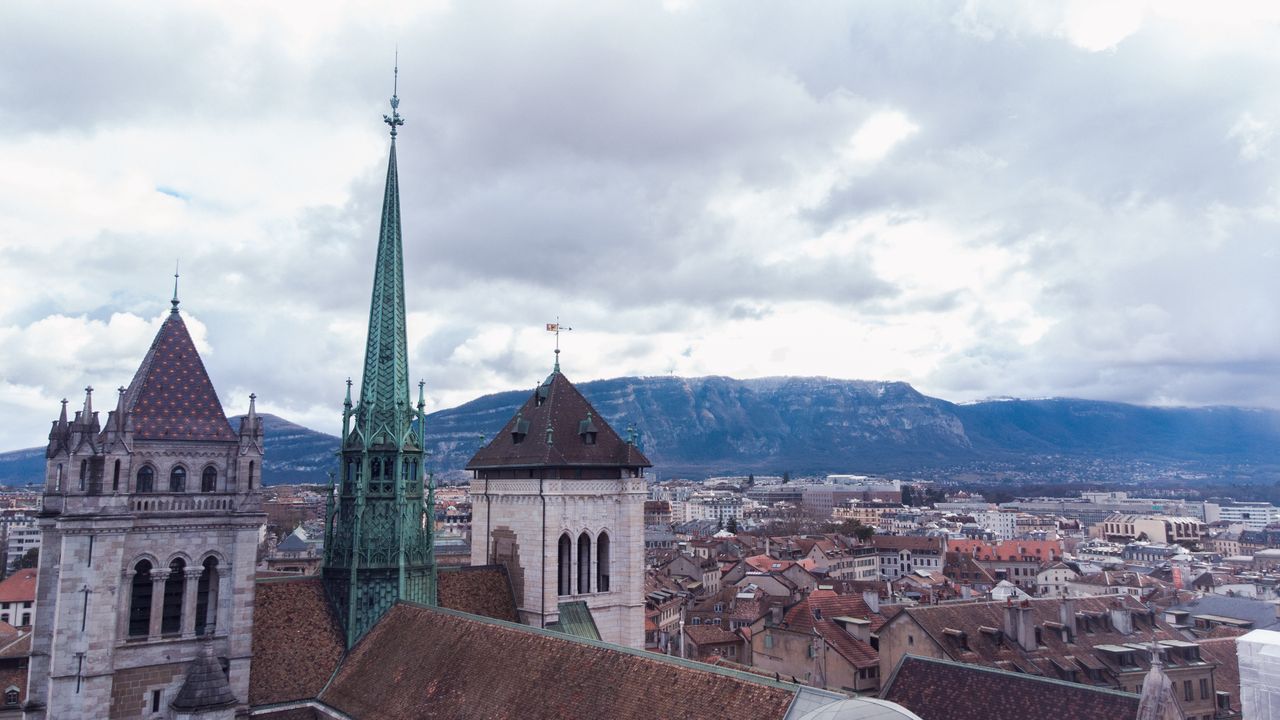 Aerial view of St. Peters Cathedral in Geneva against a mountainous backdrop on a cloudy day.